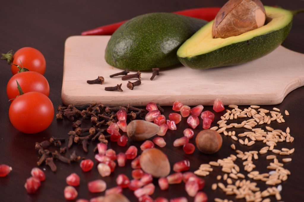 avocado sliced in half on wooden cutting board with nuts and vegetables dietary myths
